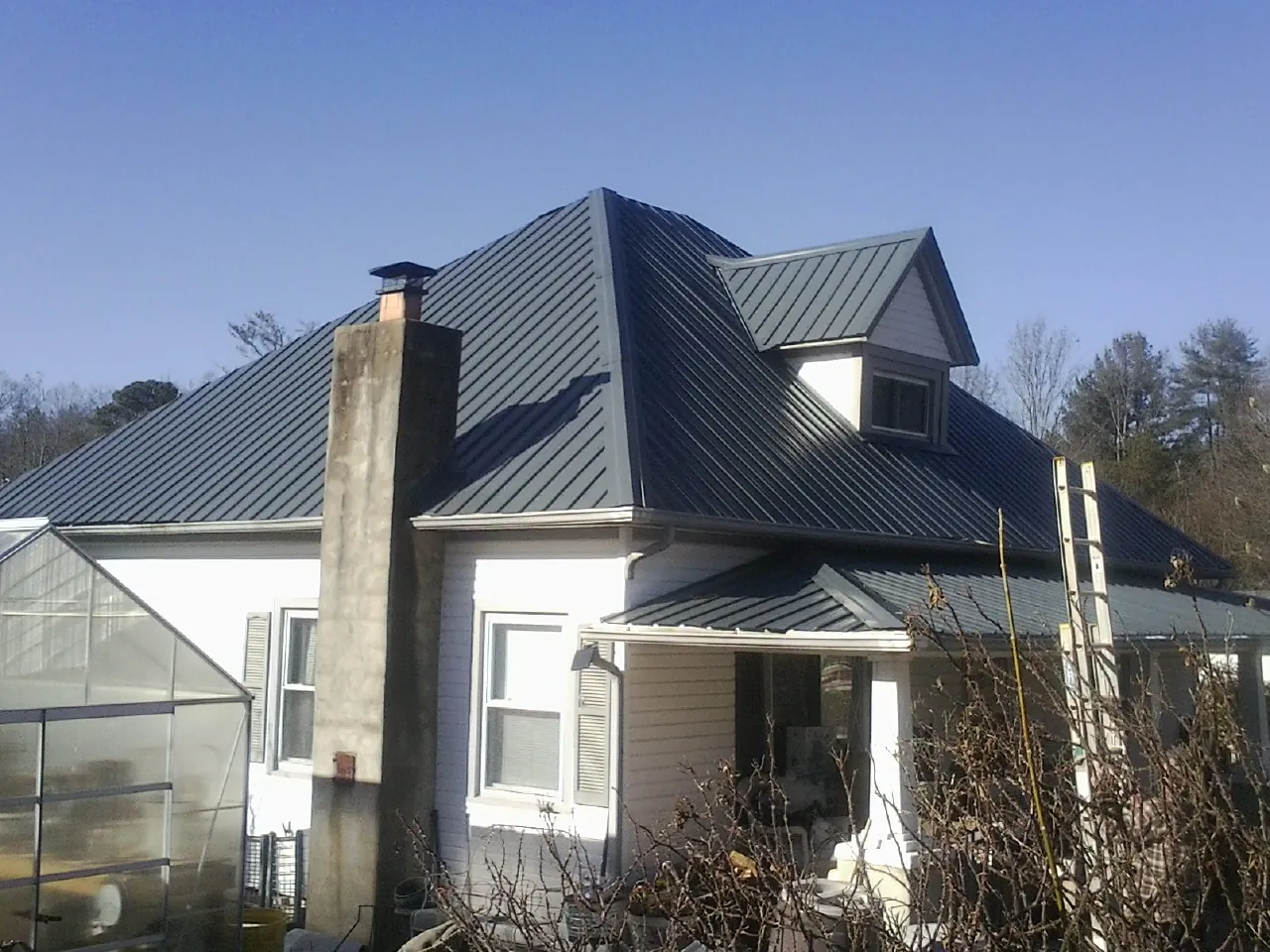 Dark blue standing seam metal roof on a white farmhouse with dormer — Slate & Tile Roof Repair by Roofing Brothers in Bay Pines