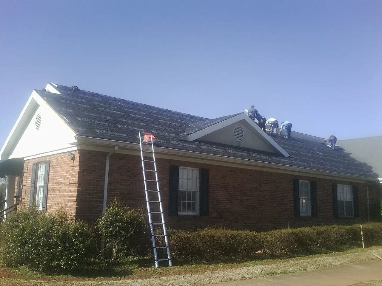 Crew tearing shingles off a brick ranch roof with a ladder set — Metal Roof Repair work by our crew in Bay Pines