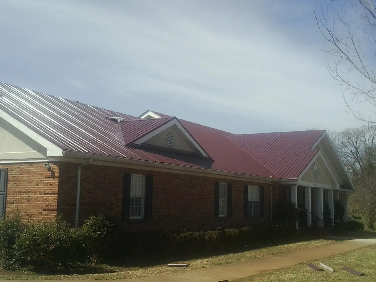 Red metal roof with gabled entries on a long brick building, from a Hail Damage Roof Repair job in Bay Pines