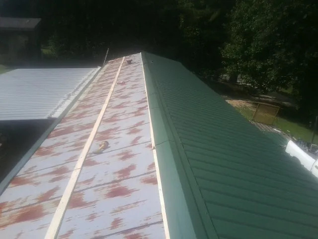 Old rusted panels beside newly installed green metal roofing — Wind Damage Roof Repair by Roofing Brothers in Bay Pines