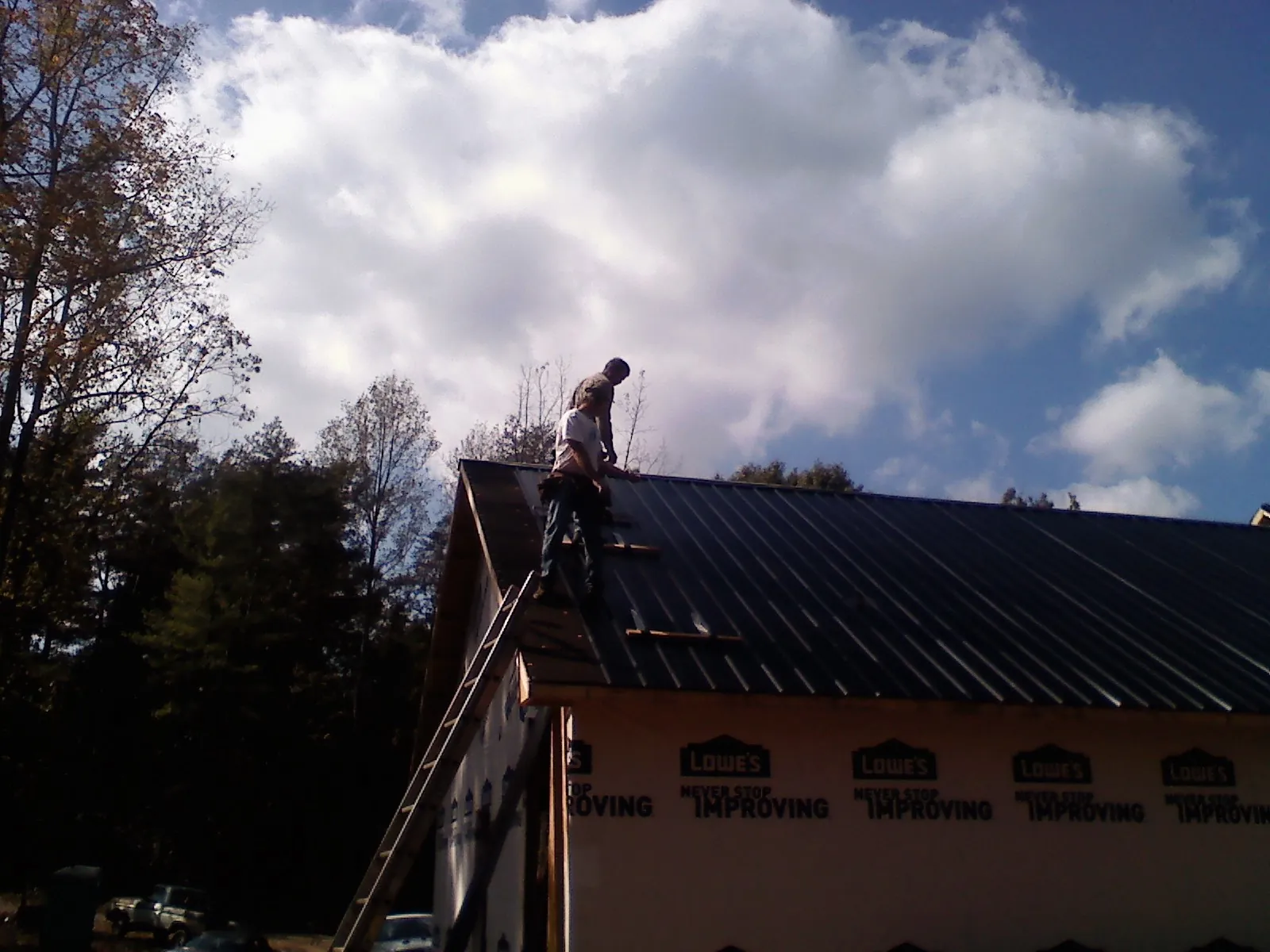 Roofer fastening dark metal panels high against a cloudy sky, from a Roof Inspection job in Bay Pines
