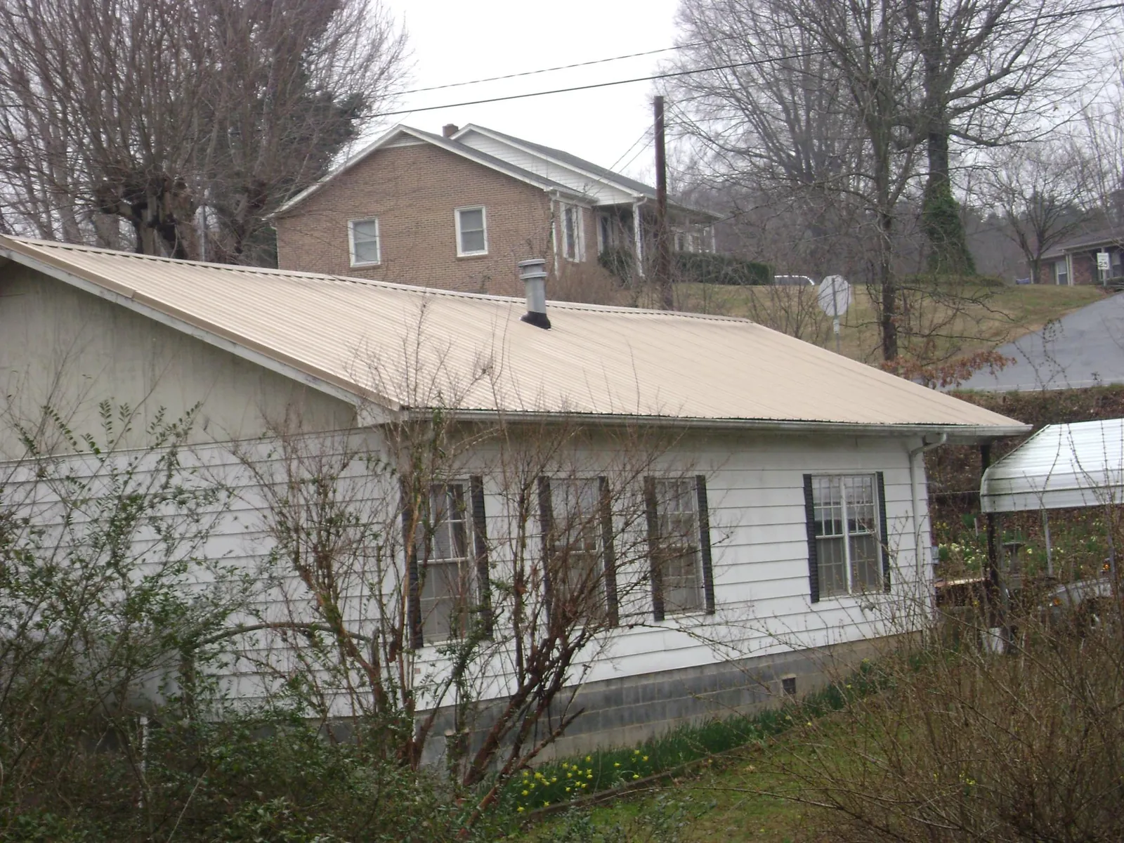 Tan metal roof on a white sided house set into a hillside — Commercial Roofing by Roofing Brothers in Bay Pines
